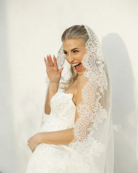 Nicole on her wedding day, in a lace veil, laughing and waving.